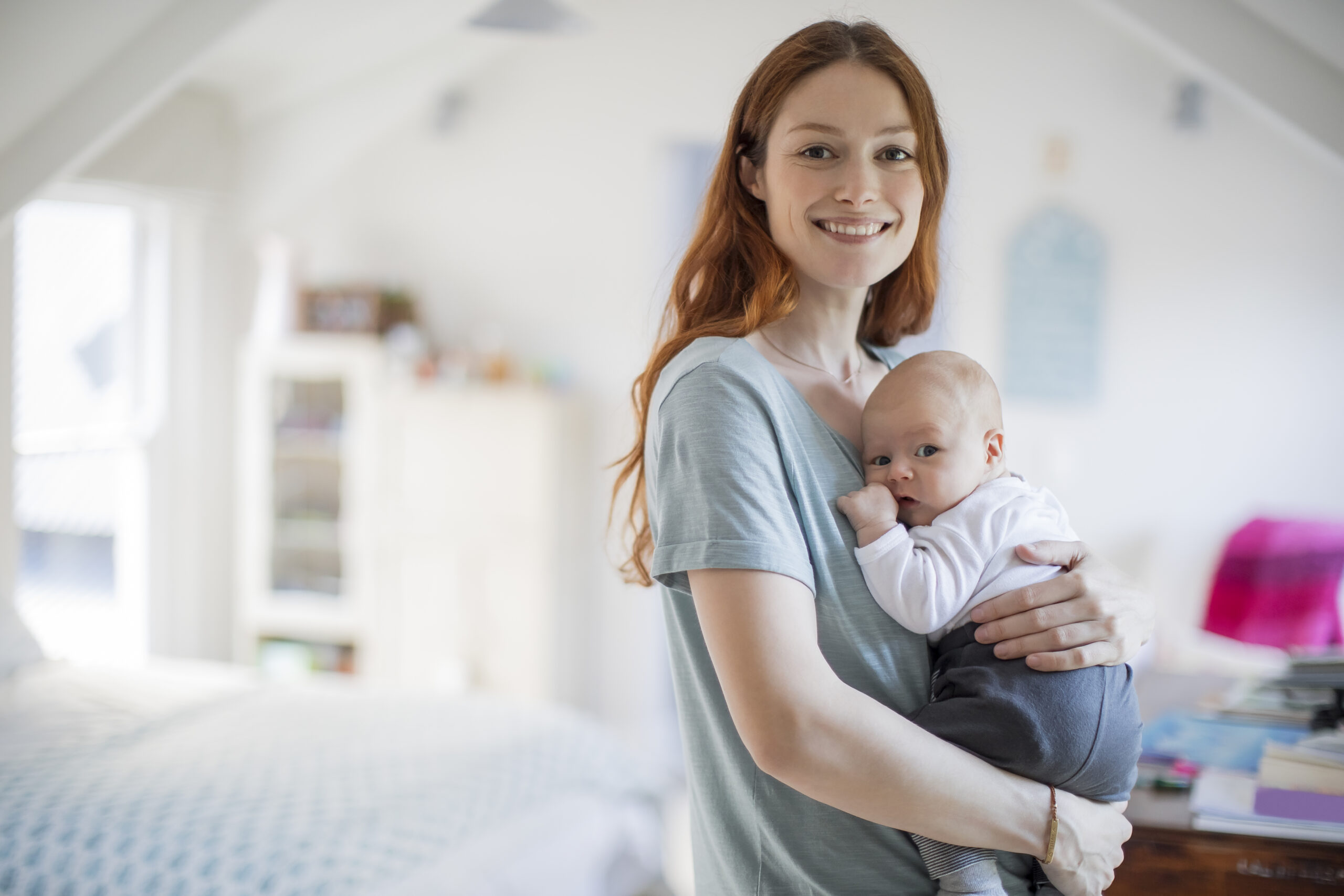Smiling redhead mother carrying son at home