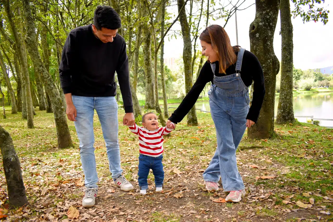 Parents helping their young child walk in a park, representing modern co-parenting and family life.